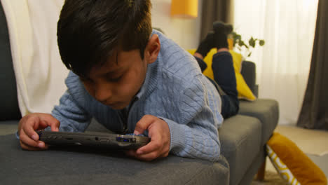 Young-Boy-Lying-On-Sofa-At-Home-Playing-Game-Or-Streaming-Onto-Handheld-Gaming-Device-5